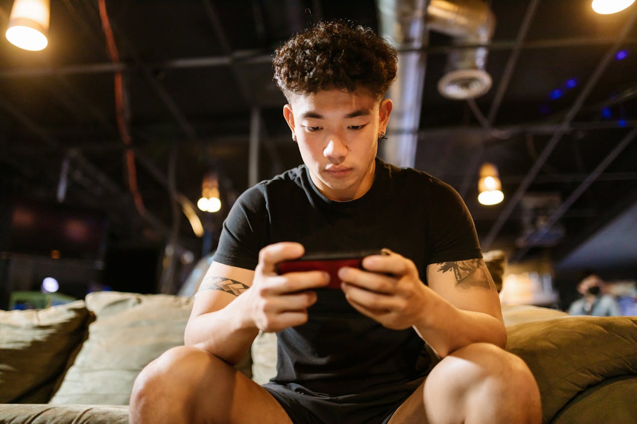 Focused young man engaged in gaming on smartphone indoors, enjoying online recreation.